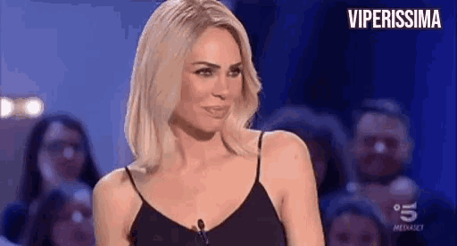 a woman in a black tank top is talking into a microphone on a tv show .