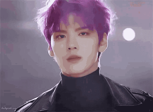 a man with purple hair is wearing a black turtleneck and a leather jacket .