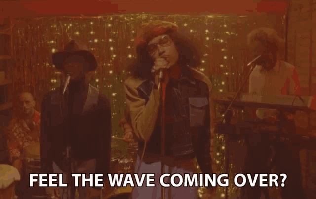 a man singing into a microphone with the words " feel the wave coming over " above him