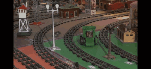 a toy train set with a green tractor on the tracks and the number 3 on the ground