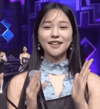 a woman is holding a microphone and smiling while standing in front of a purple background .