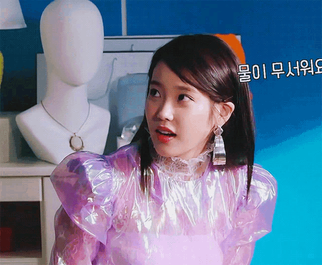 a woman wearing a purple top and silver earrings is standing in front of a mannequin