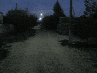 a dirt road at night with a house in the distance