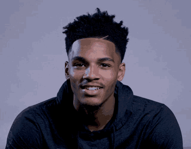 a man wearing a black hoodie smiles for the camera