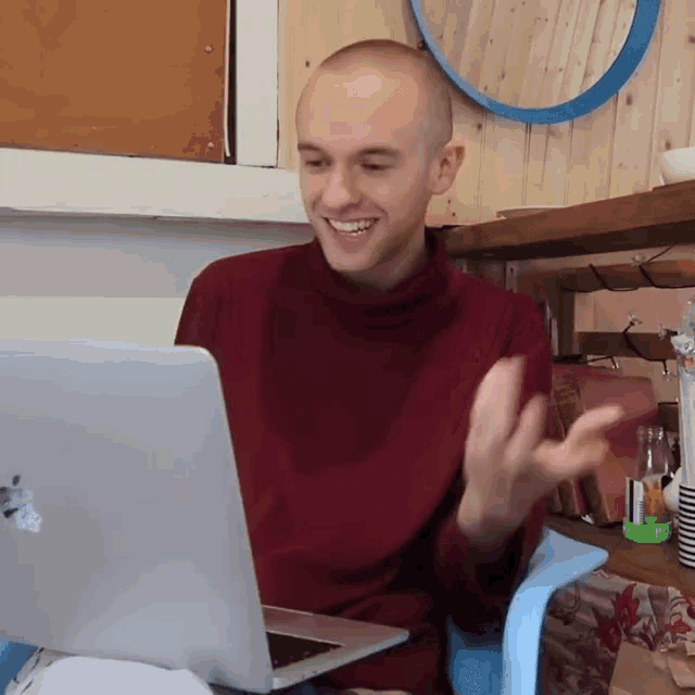 a man in a red sweater is smiling while looking at a laptop