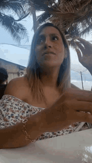 a woman is sitting at a table in front of a palm tree wearing a bracelet .