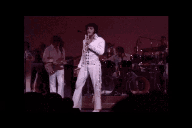 a man in a white suit is singing into a microphone on stage