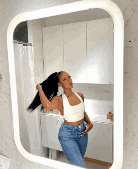 a woman adjusts her hair in front of a square mirror