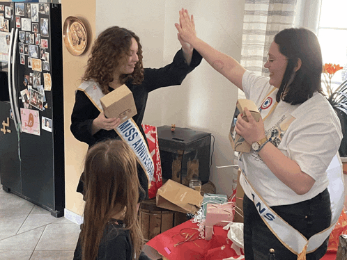a woman wearing a sash that says miss anniversaire gives a high five to another woman