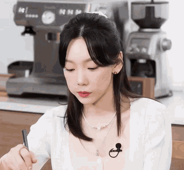 a woman is sitting in front of a coffee machine and writing on a piece of paper with a pen .