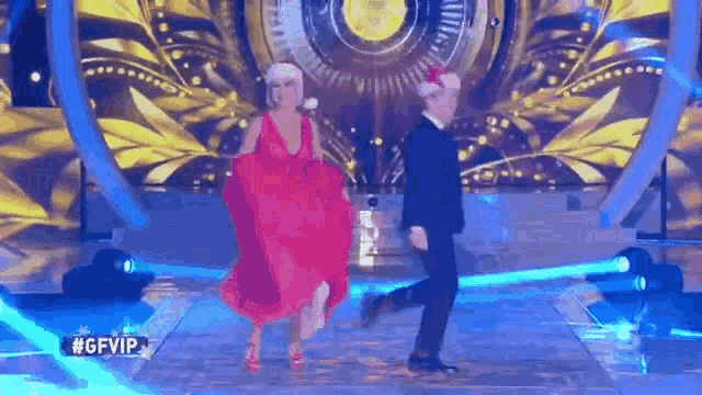 a man and a woman are dancing on a stage . the woman is wearing a santa hat and a red dress .
