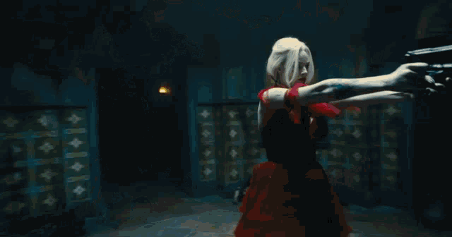 a woman with blonde hair is holding a gun in a dark room