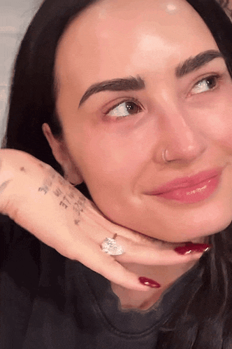 a close up of a woman 's face with a nose ring and a ring on her finger