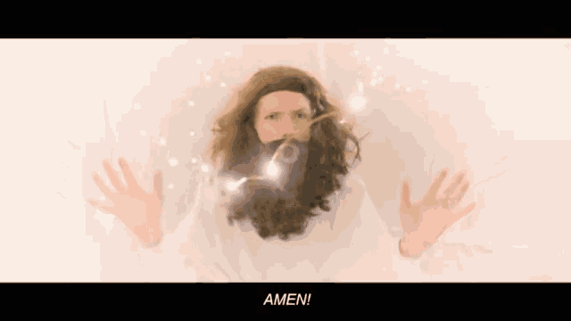 a woman with a beard and a white shirt says amen with her hands outstretched