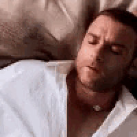 a man is laying on a bed with his eyes closed and his shirt open .