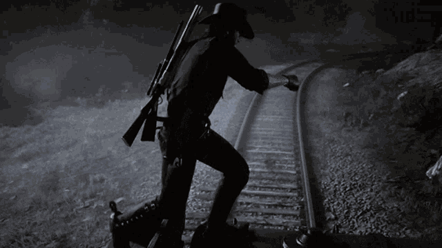 a man in a cowboy hat stands on train tracks holding a gun