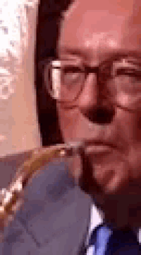 a close up of a man wearing glasses and a blue tie playing a trumpet .