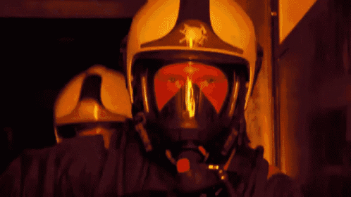 a person wearing a gas mask stands in front of a fire