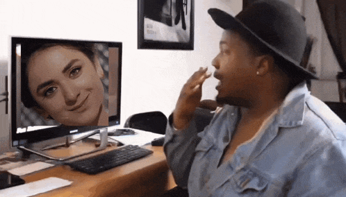a woman wearing a hat is sitting in front of a computer screen with a picture of a woman on it