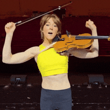 a woman in a yellow tank top is holding a violin