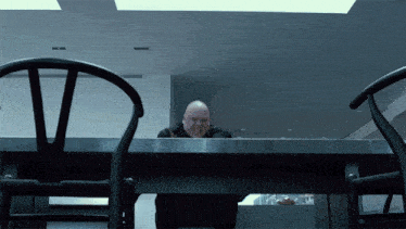 a man is sitting at a table with a chair in front of him with the letter v on it