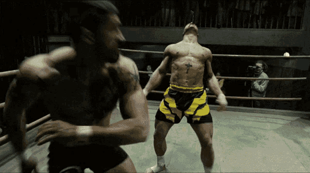 a man with a cross tattoo on his chest is in a boxing ring with another man