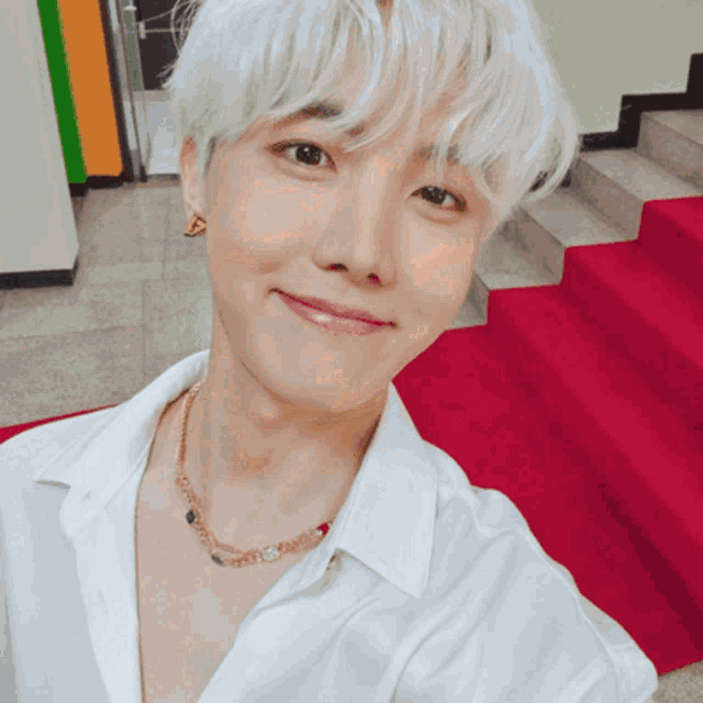 a young man wearing a white shirt and a gold necklace smiles for the camera