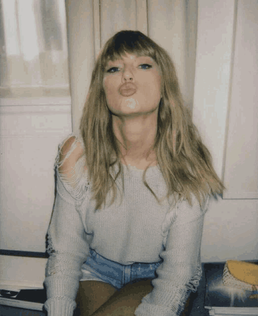 a woman wearing a sweater and denim shorts blows a kiss