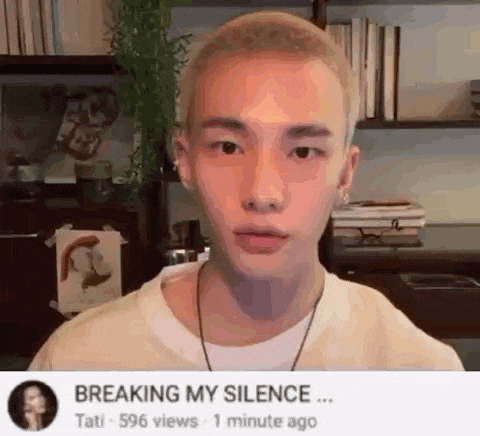 a young man with a shaved head is standing in front of a bookshelf and looking at the camera .