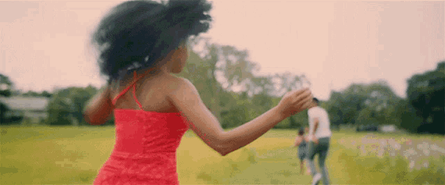 a woman in a red dress is running through a field with a man and a child behind her .