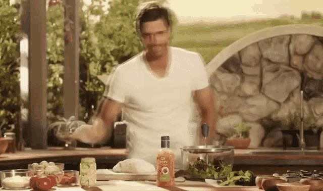 a man in a white shirt is standing in a kitchen with a bottle of olive oil