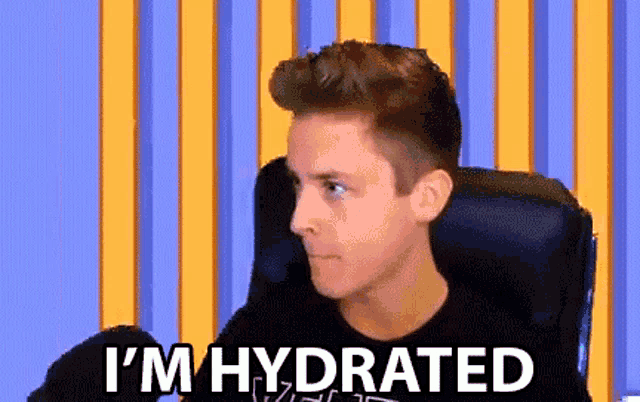 a man is sitting in a chair with the words i 'm hydrated on the screen behind him .
