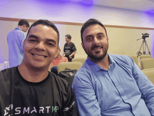 two men are posing for a picture with one wearing a smartmp shirt