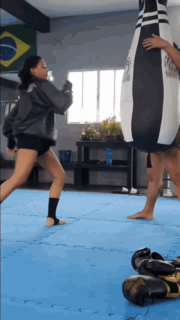a woman in a gray jacket is kicking a punching bag that says ' ufc ' on it