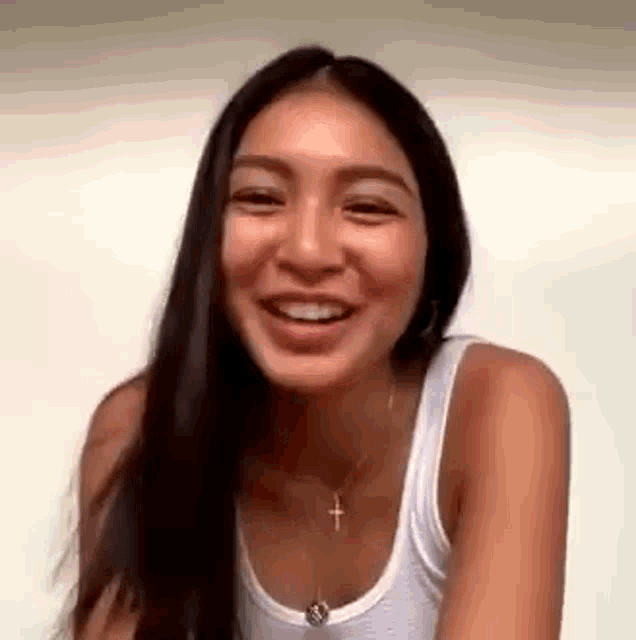 a woman with long hair is wearing a white tank top and a cross necklace .