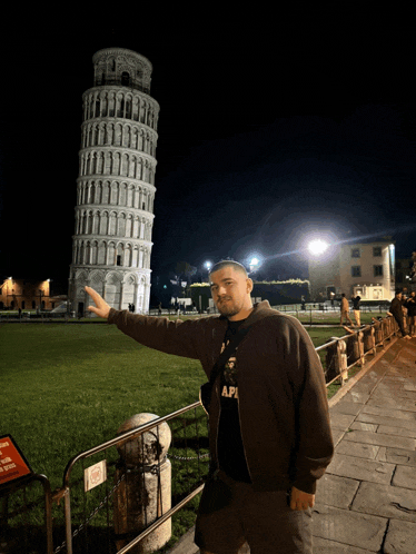 a man wearing a black shirt that says api stands in front of a very tall building