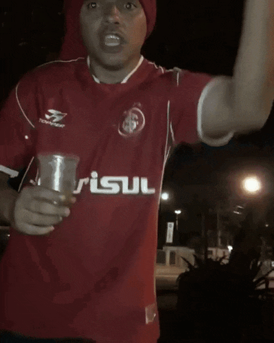 a man wearing a red topper jersey holds a cup in his hand