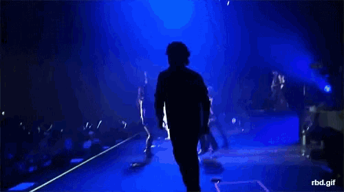 a man is standing on a stage with a blue light behind him and the words rbd.gif below him