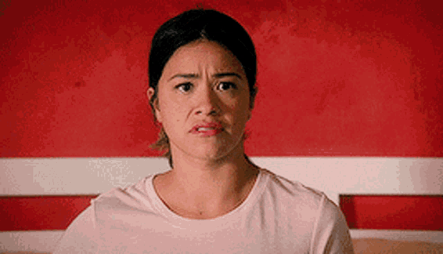 a woman in a pink shirt is making a funny face in front of a red wall