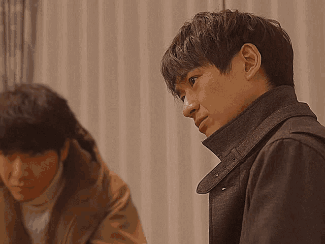 a man in a black coat looks at another man in a tan coat