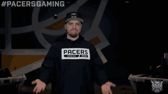 a man wearing a pacers gaming hoodie stands in front of a wall