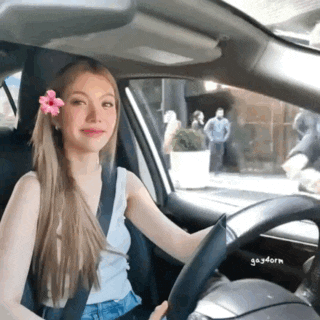 a woman is driving a car with a flower in her hair