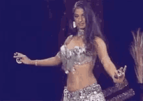 a belly dancer is dancing on a stage in a silver outfit .