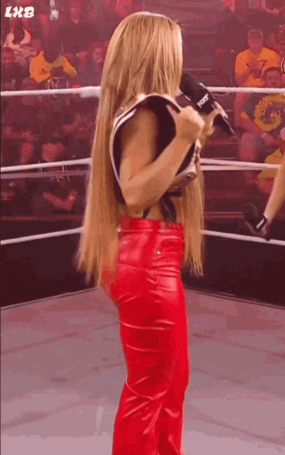 a woman in red leather pants stands in a wrestling ring holding a microphone