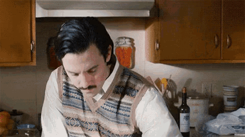 a man with a mustache is cooking in a kitchen with a bottle of wine in front of him