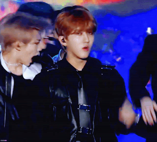 a group of young men are standing on a stage and one of them is wearing a black jacket .