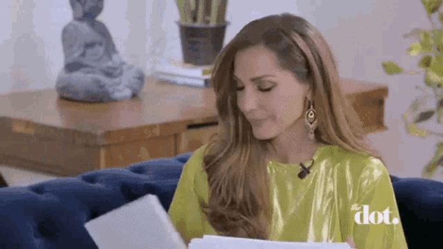 a woman is sitting on a blue couch reading a book with the word dot on her shirt