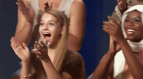 a group of women are clapping their hands in the air while sitting in a stadium .