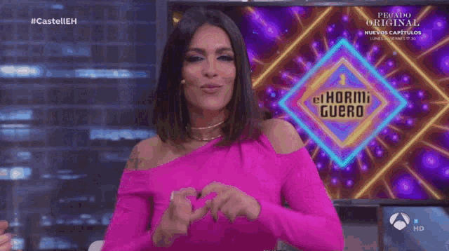 a woman is making a heart shape with her hands in front of a sign that says el hormiguero