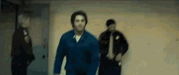 a man in a blue jacket is walking down a hallway with two men .